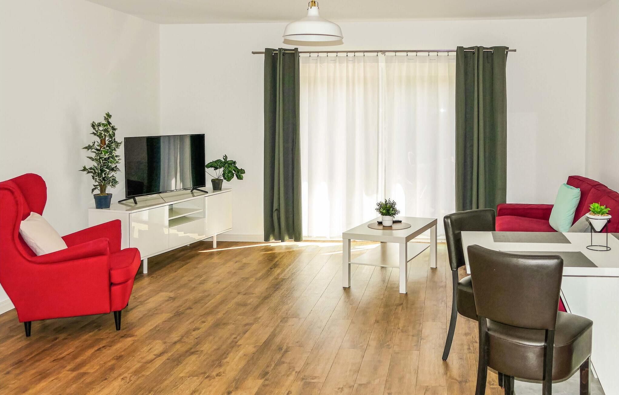 Una sala moderna con un sofá rojo, un sillón de cuero negro, un mueble blanco para televisor y una mesa de comedor con sillas.
