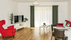 Een moderne woonkamer met een rode bank, een zwarte leren fauteuil, een witte tv-kast en een eettafel met stoelen.