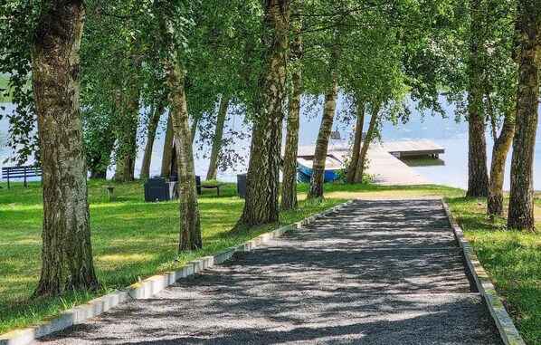 Stroll along the serene pathway to a tranquil dock area surrounded by lush greenery and trees, with benches for relaxation and a small structure in the distance.