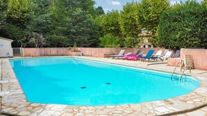A swimming pool with a stone border, surrounded by lounge chairs and a stone deck. - Lovely apartment in Rustrel (Rustrel)