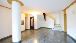 A spacious hallway with a marble floor, a large white pillar, and a staircase leading to an upper level.