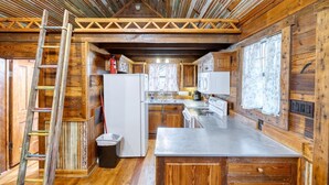 A rustic kitchen with wooden walls, a central island, and a ladder leaning against the wall. - Unique Cabin by the Frio - River Rock Cabin #3 (Concan)