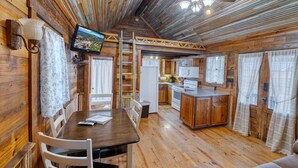 A cozy cabin-style kitchen with wooden walls, a dining table, and a ceiling fan. - Unique Cabin by the Frio - River Rock Cabin #3 (Concan)