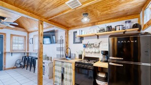 A compact kitchen with a Galanz refrigerator, a stove, and a sink. There are wooden beams on the ceiling, and a fan is visible in the corner. - Tiny home by the Frio River - River Rock Cabin #4 (Concan)