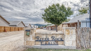 A gravel driveway leading to a stone sign with "River Rock Cabins" written on it. - Tiny home by the Frio River - River Rock Cabin #4 (Concan)