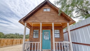 A log cabin with a porch, a blue door, and a small window. - Tiny home by the Frio River - River Rock Cabin #4 (Concan)