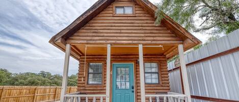 A log cabin with a porch, a blue door, and a small window.