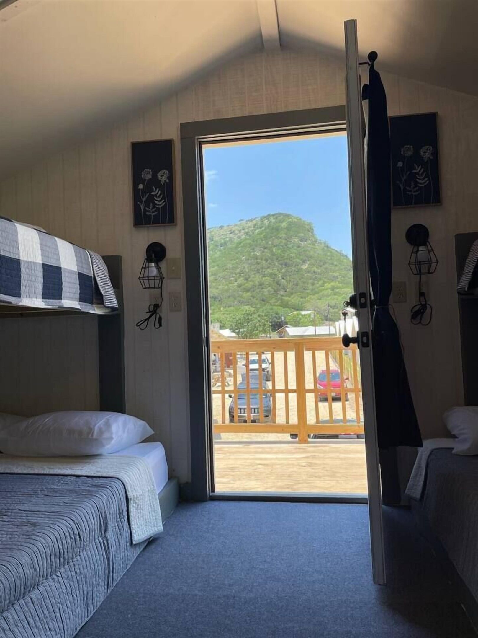 A room with a bunk bed, a desk, and a window with a view of a mountain and a wooden deck outside.