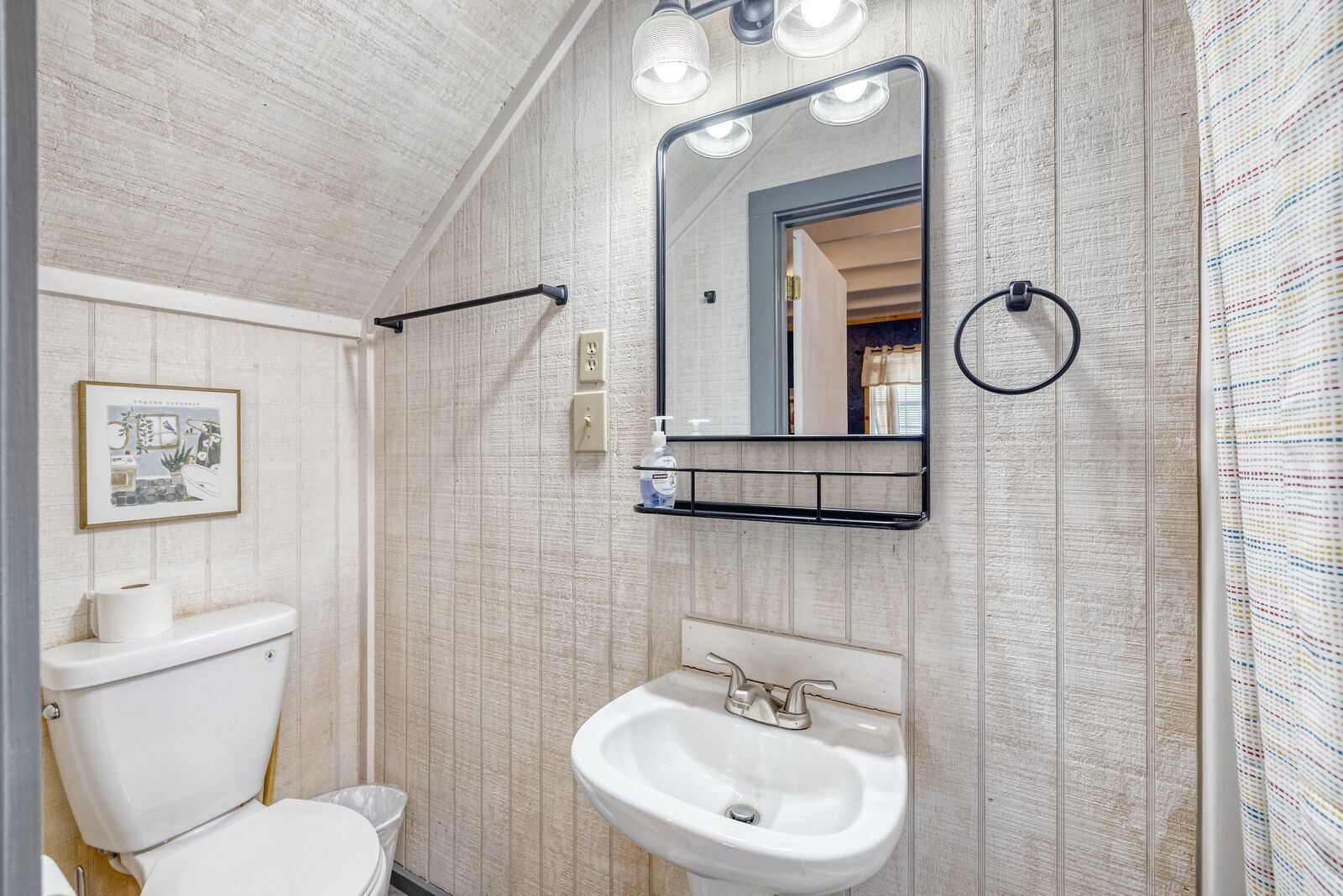 A bathroom with a toilet, sink, mirror, and towel rack.