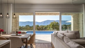 A modern living room with a large window overlooking a pool and mountains. - Beach front home in Malinska (Malinska)