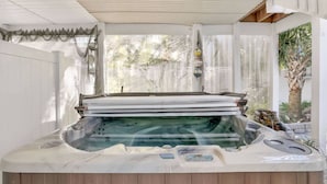 Een hottub met een houten terras, omringd door een witte hek en een overdekt gebied met een gegolfd dak.