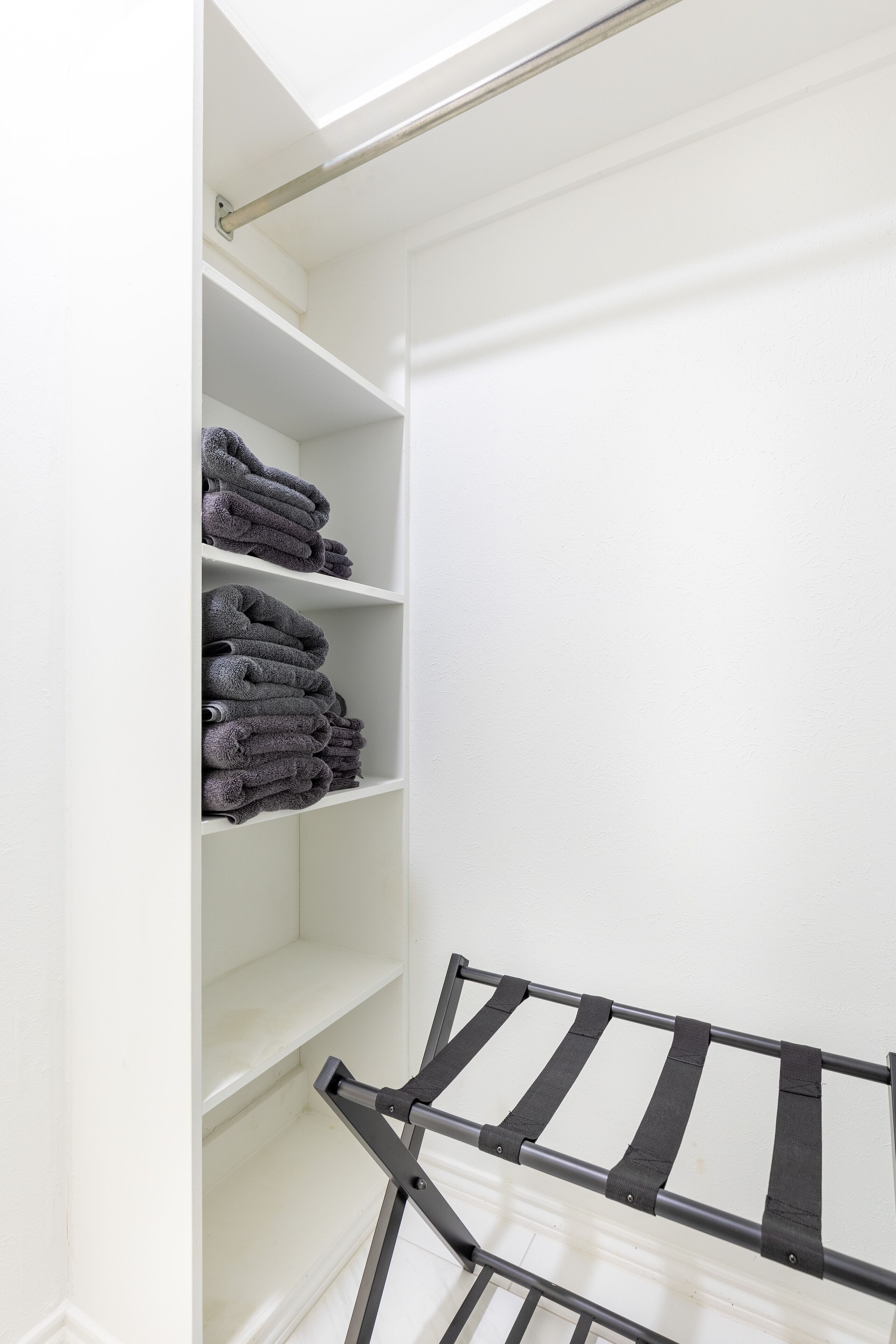 Un placard blanc avec des étagères où sont pliées des serviettes, et un étendoir noir.