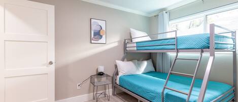 A bunk bed room with a white door, a small bedside table with a lamp, and a framed picture on the wall.