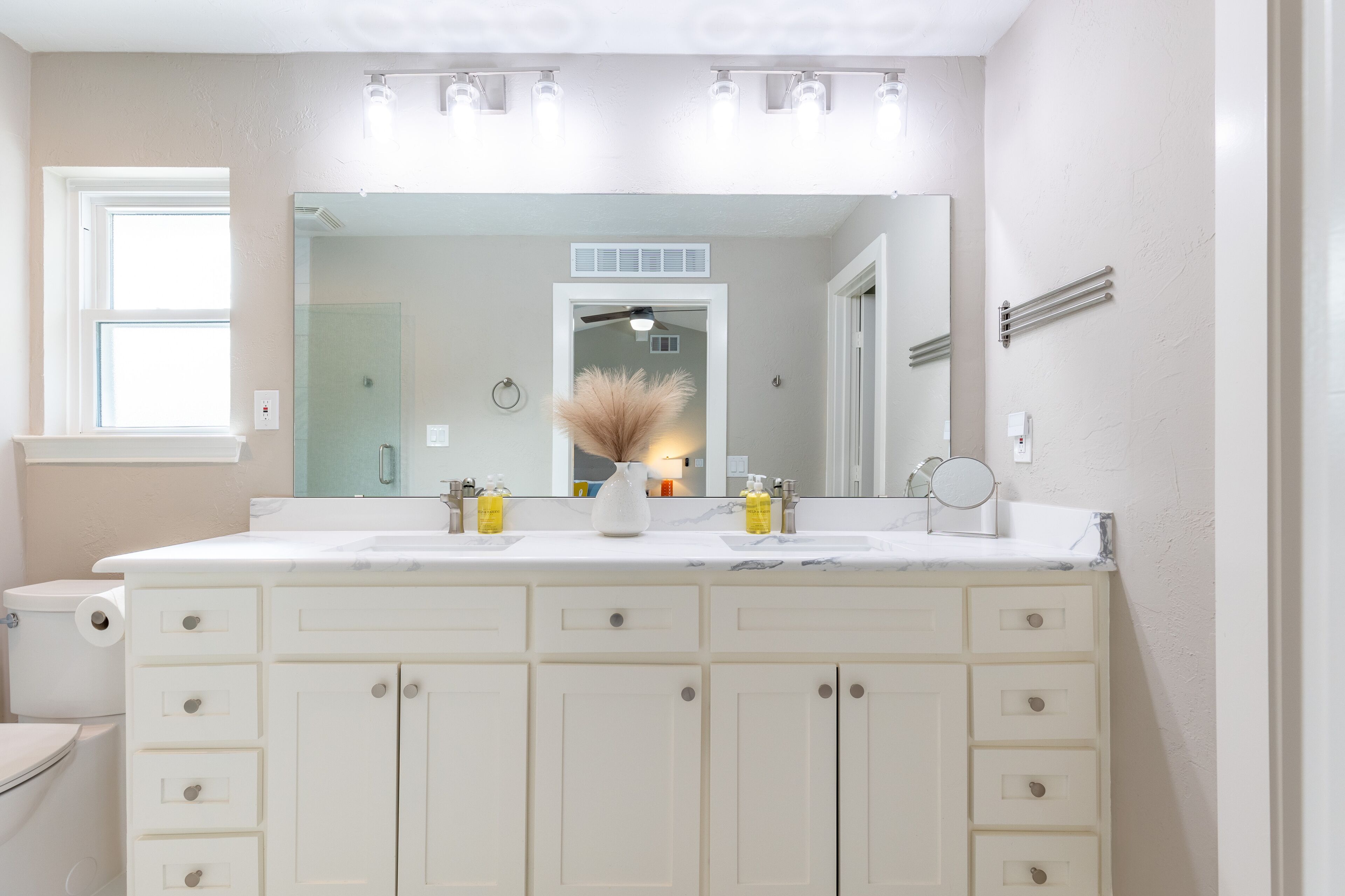 A bathroom with a large mirror, two sinks, and a vanity with drawers.