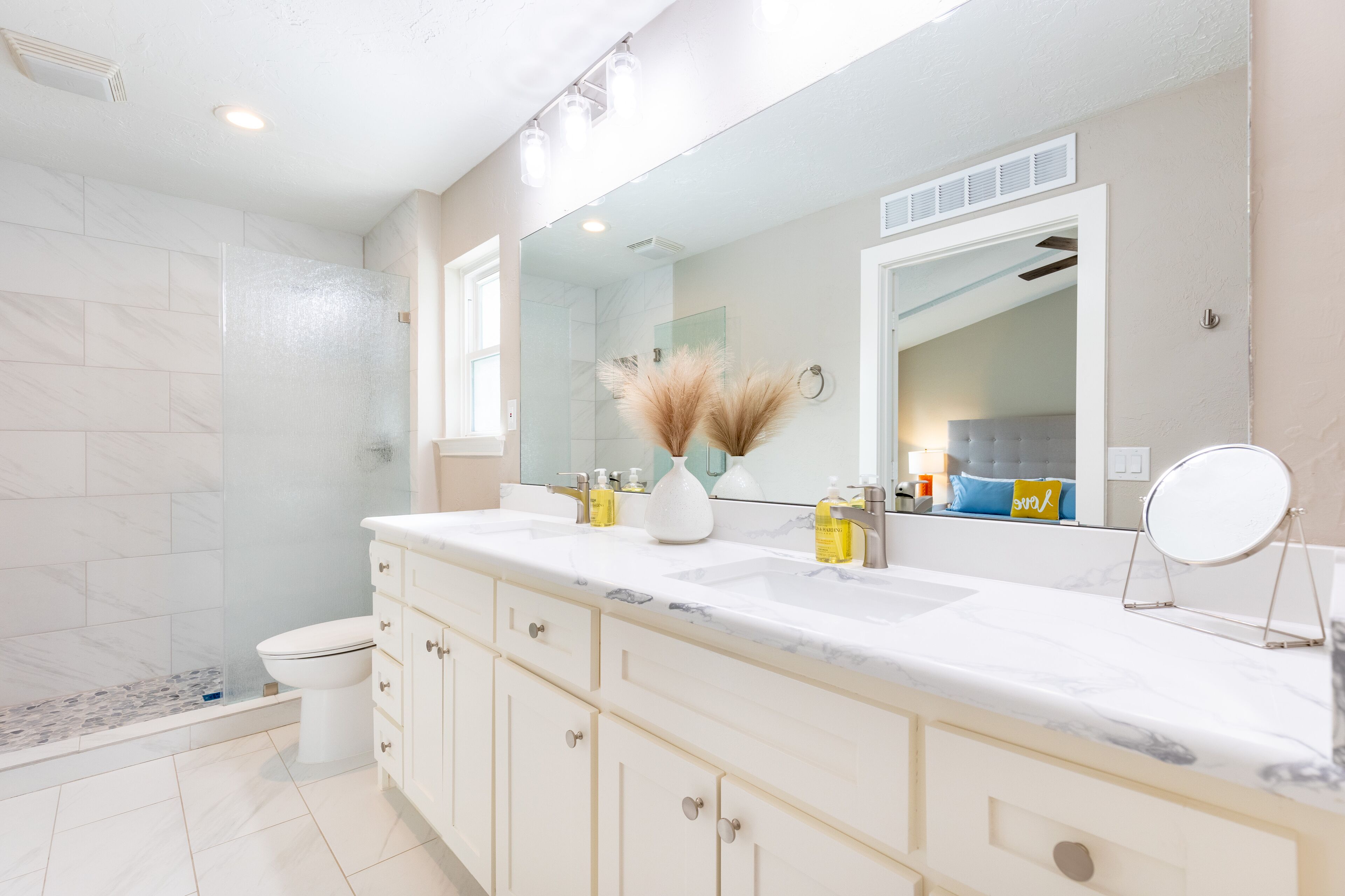 A modern bathroom with a large mirror, a shower, and a toilet.
