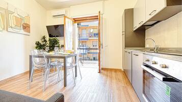 Eine moderne Küche mit Edelstahlgeräten, ein Essbereich mit klaren Stühlen und Blick auf einen Balkon.