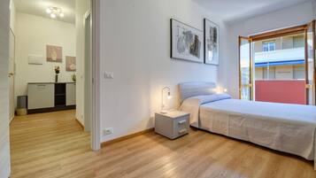Ein Schlafzimmer mit einem Bett, Nachttisch und Beistelltisch. Ein Fenster bietet Blick auf Gebäude.