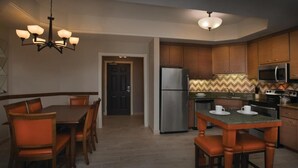 A modern kitchen with wooden cabinets, a stainless steel refrigerator, a microwave, and a dining area with a wooden table and chairs.