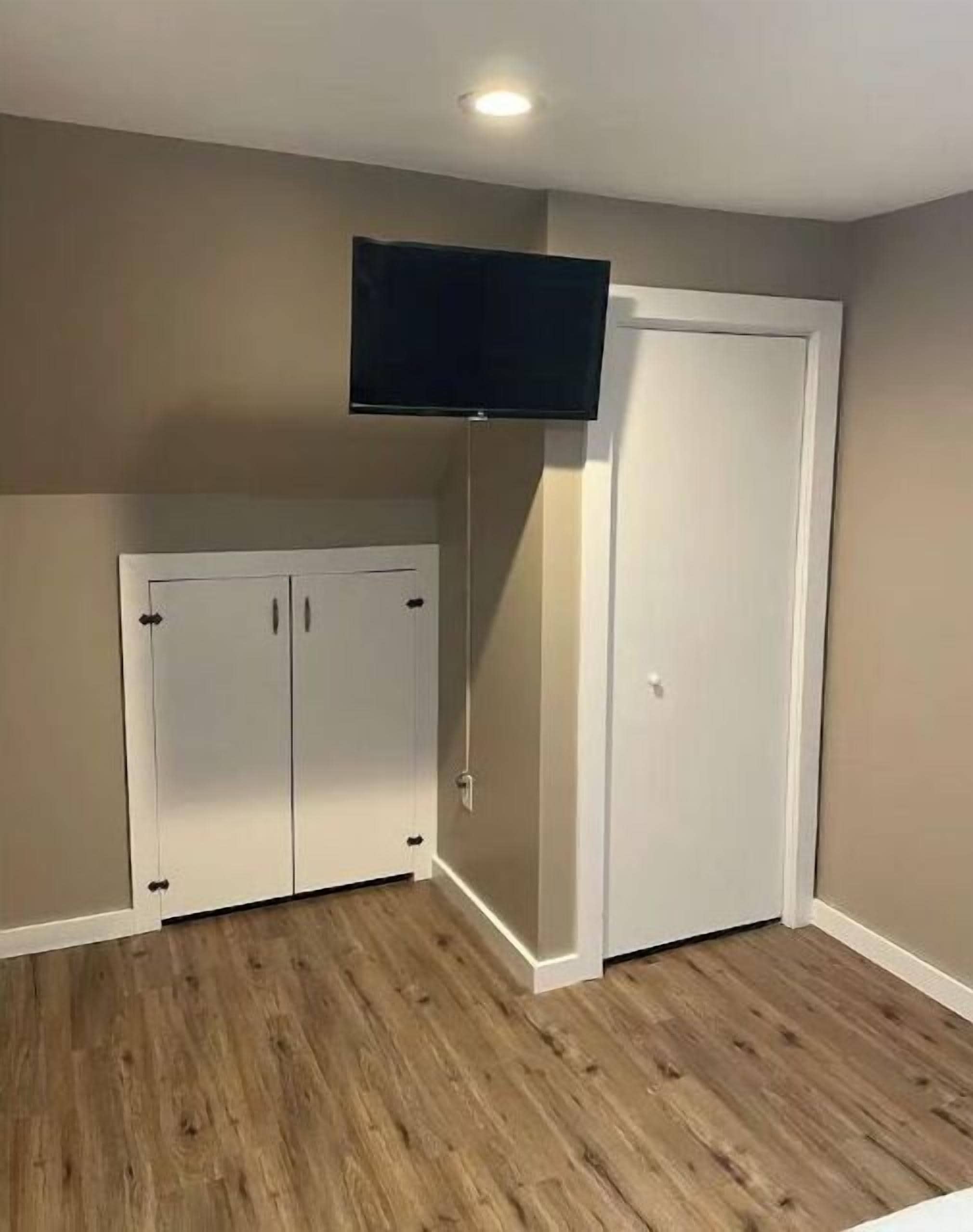 A room with a wooden floor, a white door, and a mounted television.