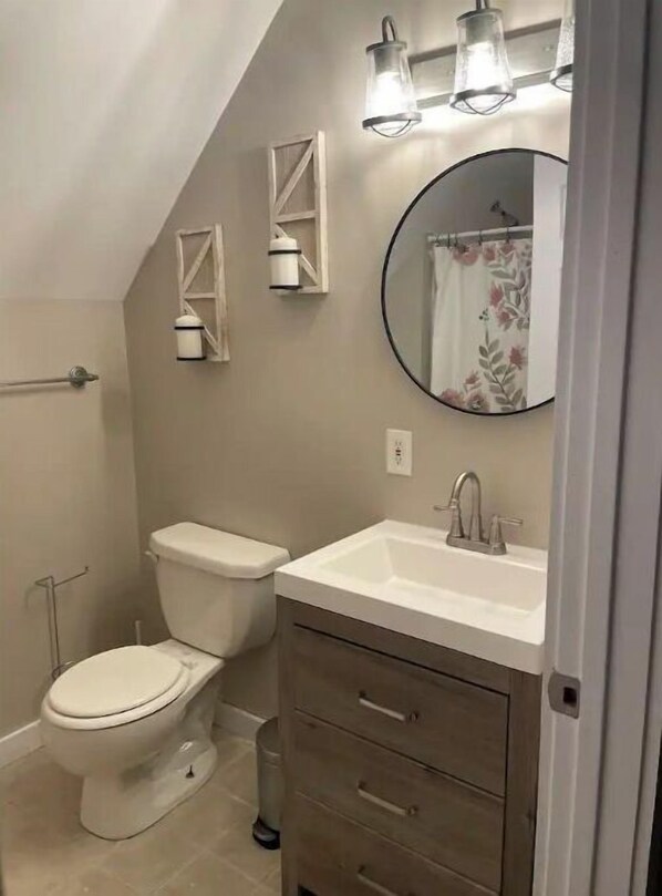 Une salle de bain comprenant des toilettes, un lavabo et un meuble-lavabo. Deux appliques murales sont fixées au-dessus du miroir.