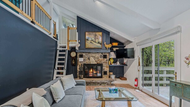 Ein geräumiges Wohnzimmer mit einem Steinkamin, einem grauen Sofa und einem Glastisch.