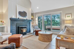 A living room with a fireplace, a sofa, a round coffee table, and a view of the outdoors.