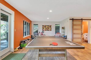 A ping pong table in a room with orange walls, a bicycle, and a wooden door.