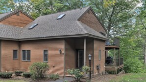 A two-story house with a covered porch, a small deck, and a front yard with landscaping. - Condo with Hot Tub & Private Sauna, Deere Run (Quechee)