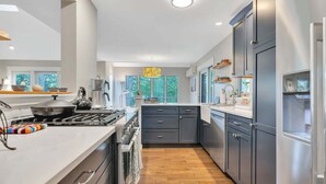 A modern kitchen with dark cabinets, a stove, and a large window. - Condo with Hot Tub & Private Sauna, Deere Run (Quechee)