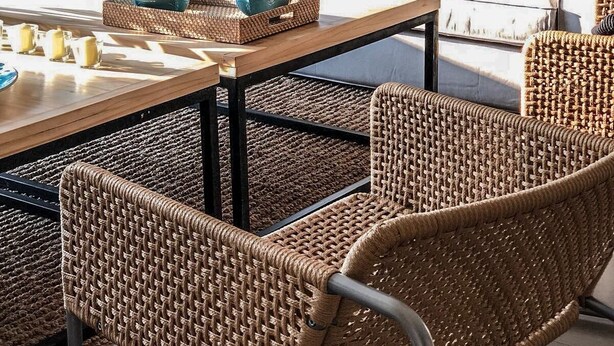 Ein modernes Wohnzimmer mit einer Couch, Korbstühlen, einem Couchtisch und Blick ins Freie.