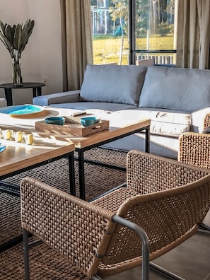 Uma sala de estar moderna com um sofá, cadeiras de vime, uma mesa de centro e vista para o exterior.