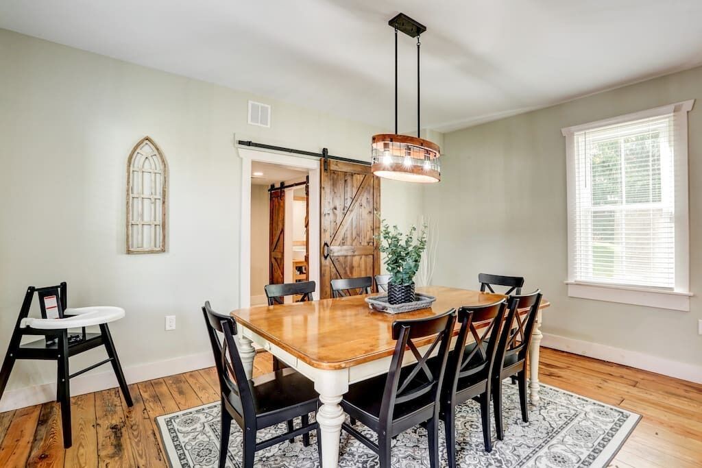 A dining area with a wooden table, black chairs, a chandelier, and a window with blinds.