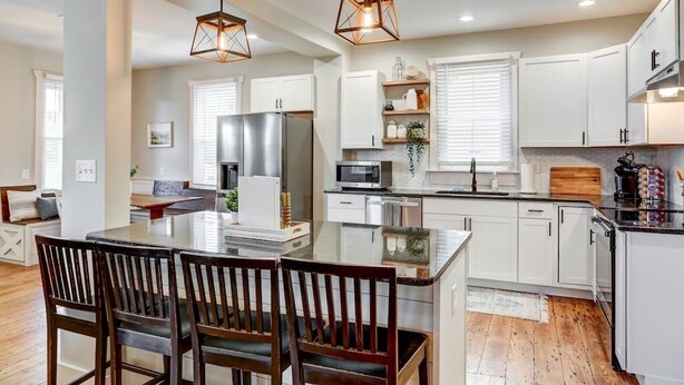 Une cuisine moderne avec des meubles blancs, un îlot central et des luminaires suspendus.