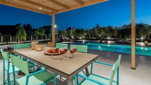Un espace extérieur aménagé pour les repas, avec une piscine, une pergola en bois et des chaises vertes.