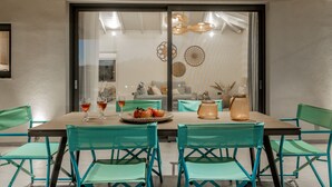 Un coin repas avec une table dressée pour deux personnes, des chaises vertes et une cloison en verre agrémentée d’œuvres d’art décoratives.