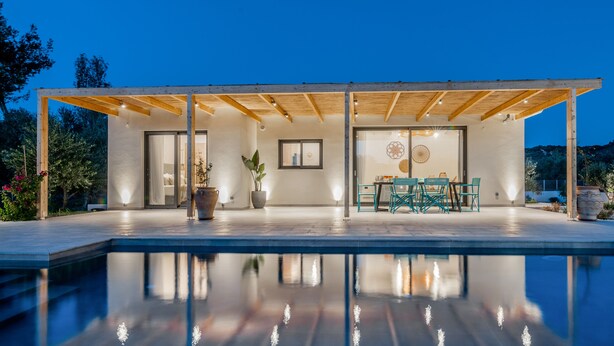 Un espace piscine extérieur moderne doté d’un patio couvert, de coins salon et offrant une vue sur le paysage environnant.