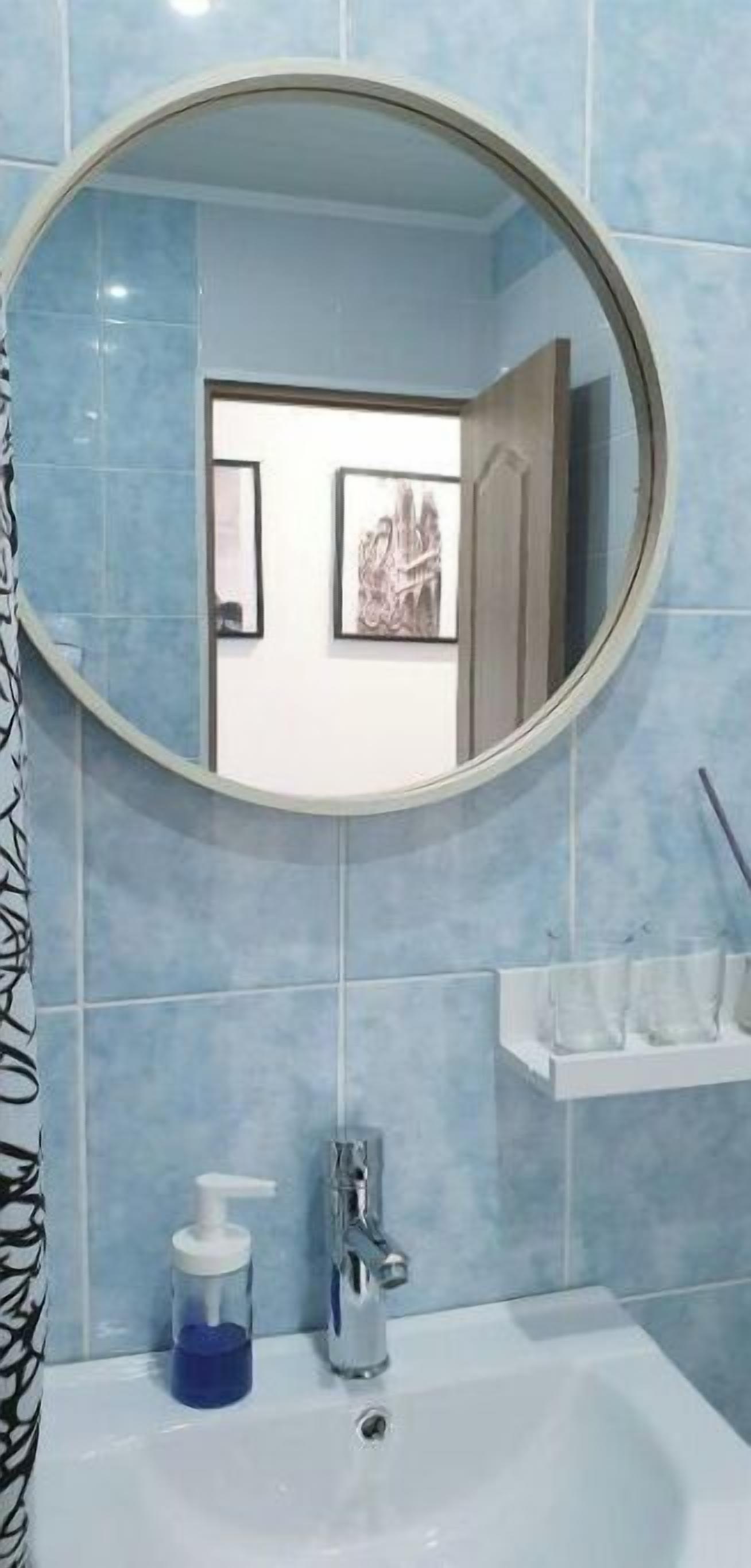 Une salle de bain avec un miroir rond, un lavabo et un distributeur de savon.