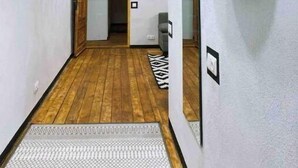 Ein Flur mit Holzboden, einem schwarzen Hängeregal und einem Spiegel an der Wand.