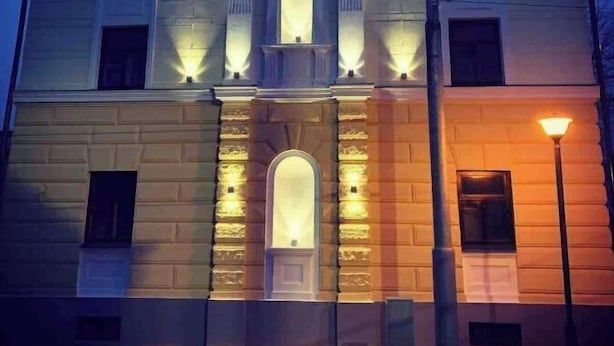 Ein großes, historisches Gebäude mit einem zentralen Rundbogenportal und zahlreichen Fenstern, beleuchtet durch Außenbeleuchtung.