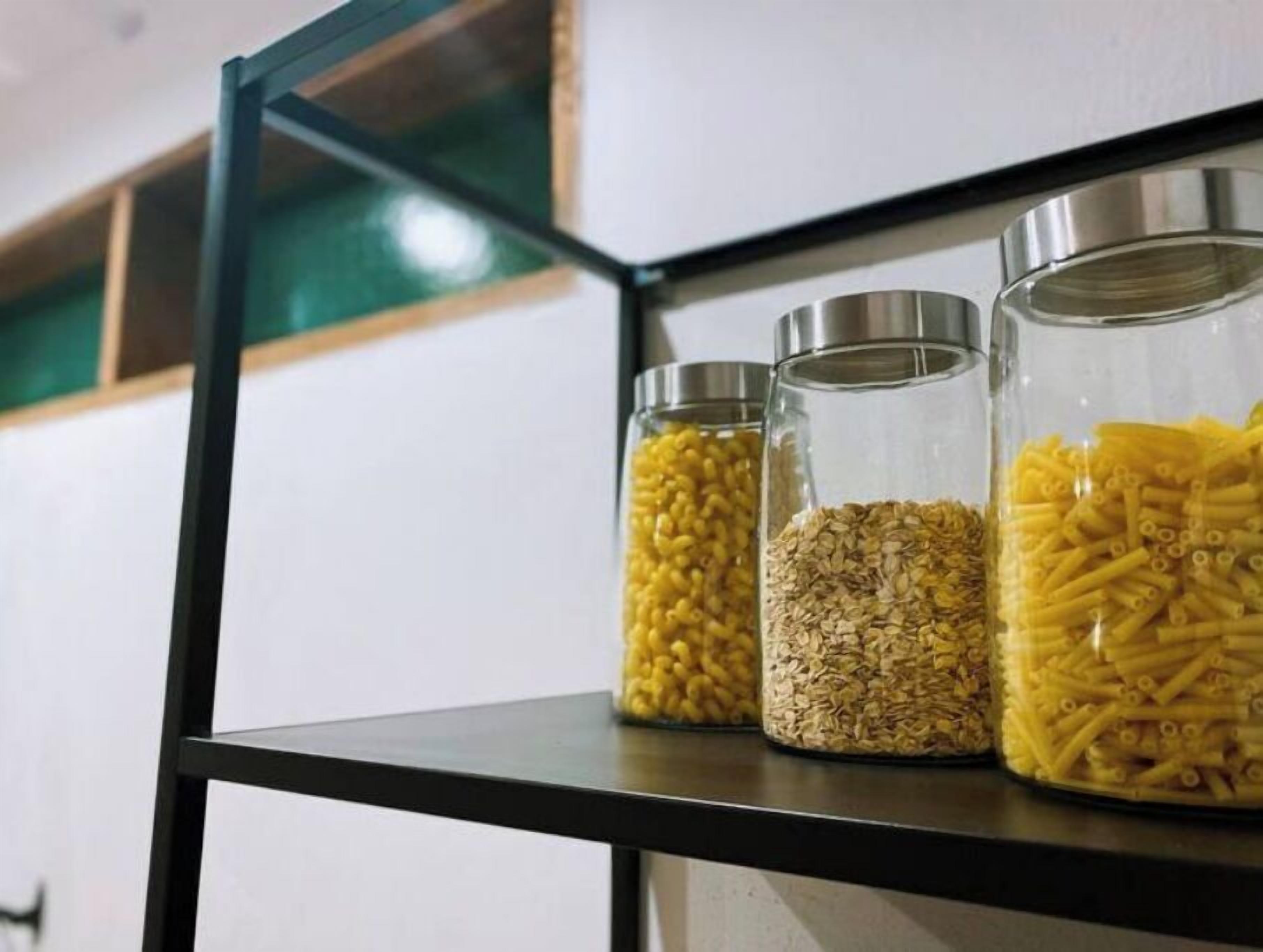 Kolme lasipurkkia, joissa on metallikannet, ja joiden sisällä on erilaisia viljoja ja pastaa. Purkit ovat mustalla hyllyllä.