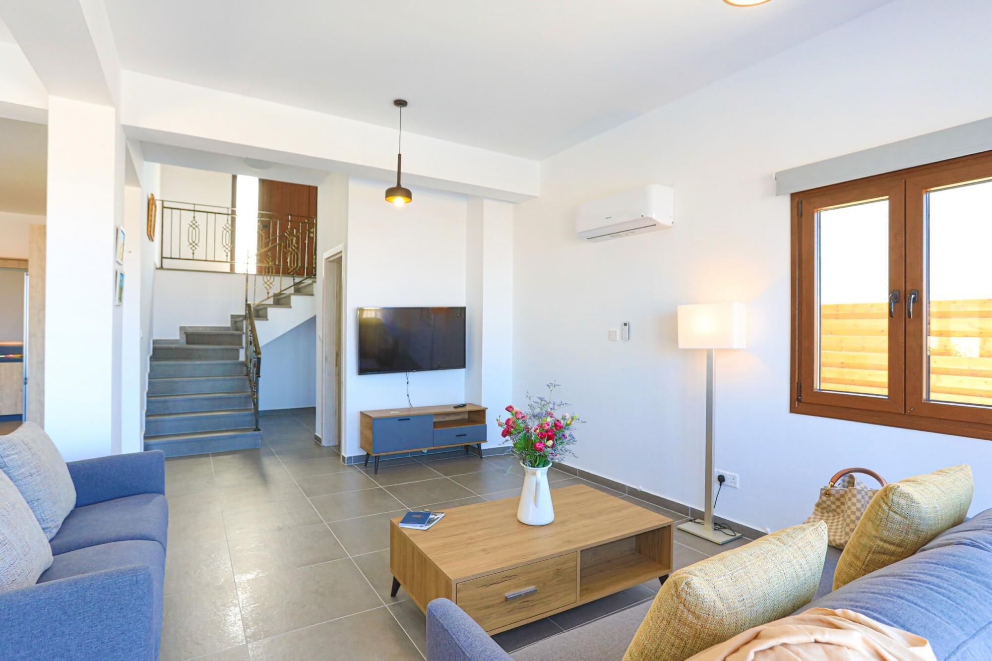 A modern living room with a sofa, a coffee table with a vase, a TV, and a staircase leading to another room.