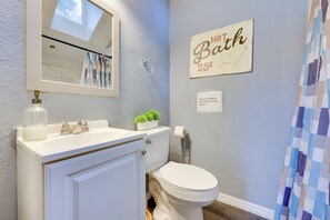 Ein Badezimmer mit einem weißen Waschbecken, einer Toilette, einem Spiegel, einer kleinen Pflanze auf dem Waschbecken, einem Handtuchhalter und einem Schild mit der Aufschrift 'HOT Bath 25¢'.