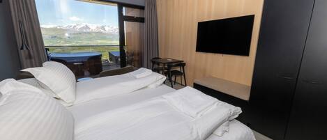 A hotel room with a large bed, a TV mounted on the wall, and a view of mountains through the window.