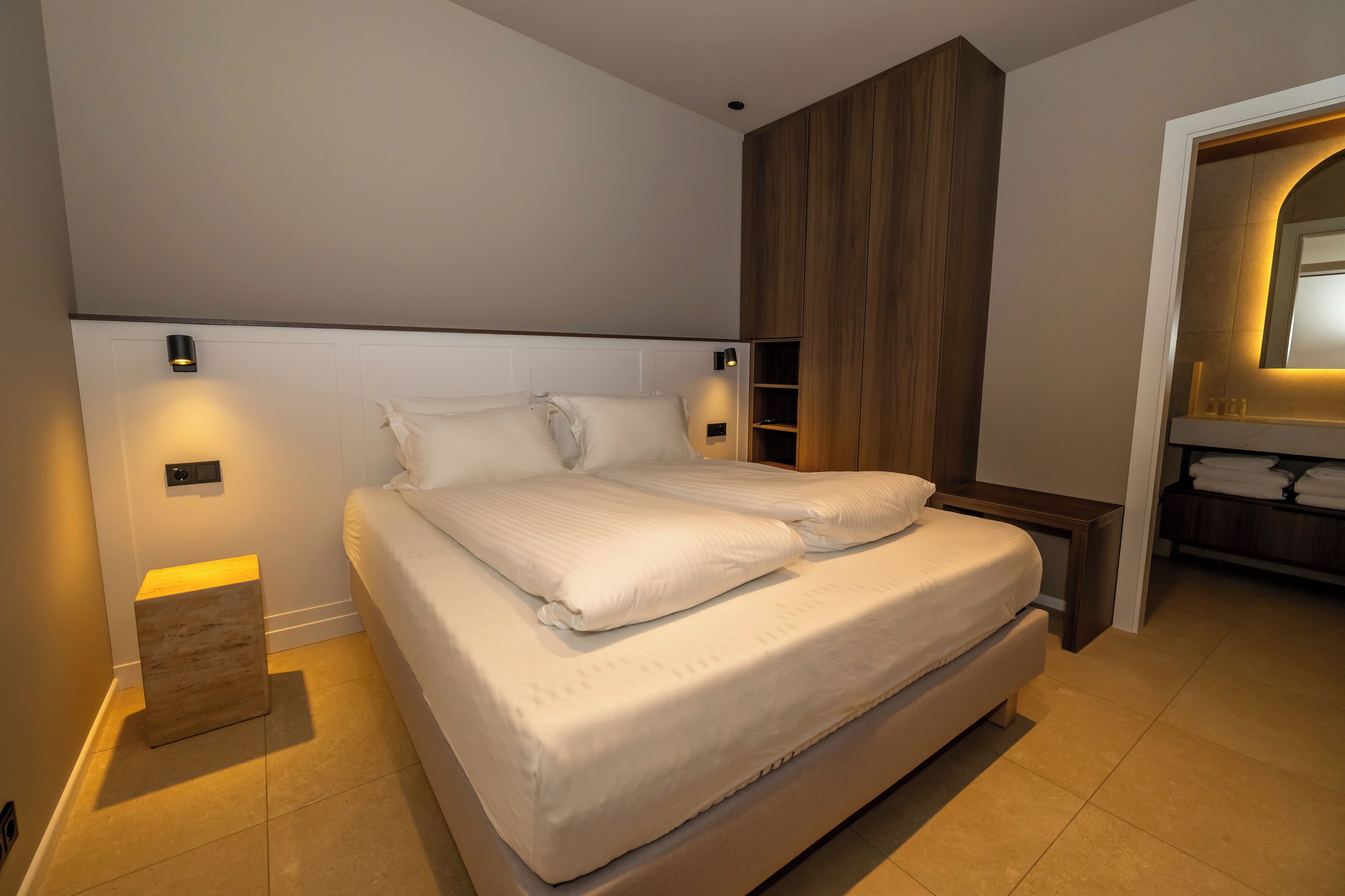 Une chambre à coucher moderne avec un grand lit, des lampes de chevet, une tête de lit en bois et une armoire intégrée.