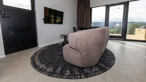 A modern room with a large window, a black door, a round rug, a grey armchair, and a small table with a lamp. - North Mountain View Suites (Akureyri)