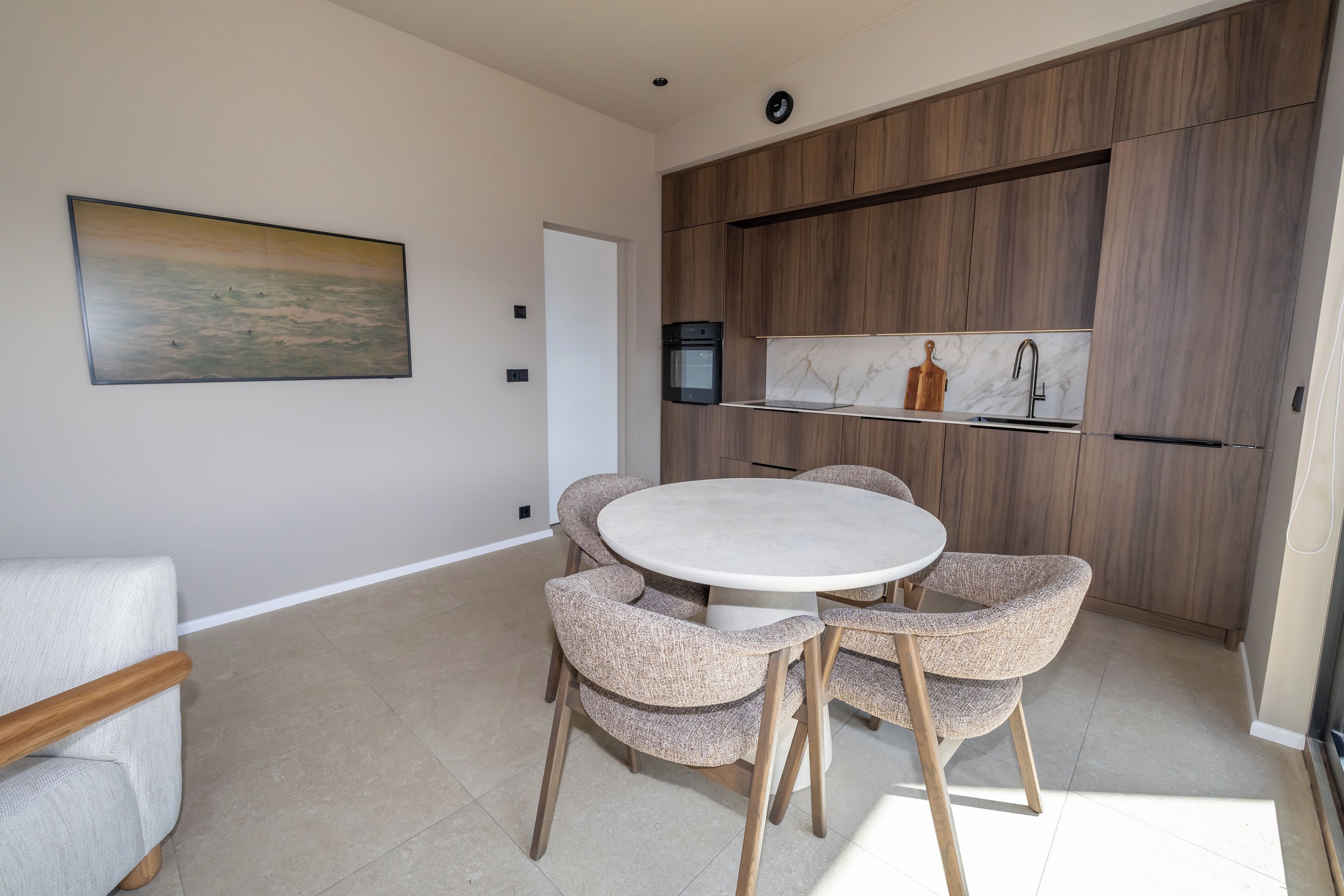 A modern kitchen with wooden cabinets, a marble backsplash, and a round dining table with upholstered chairs.