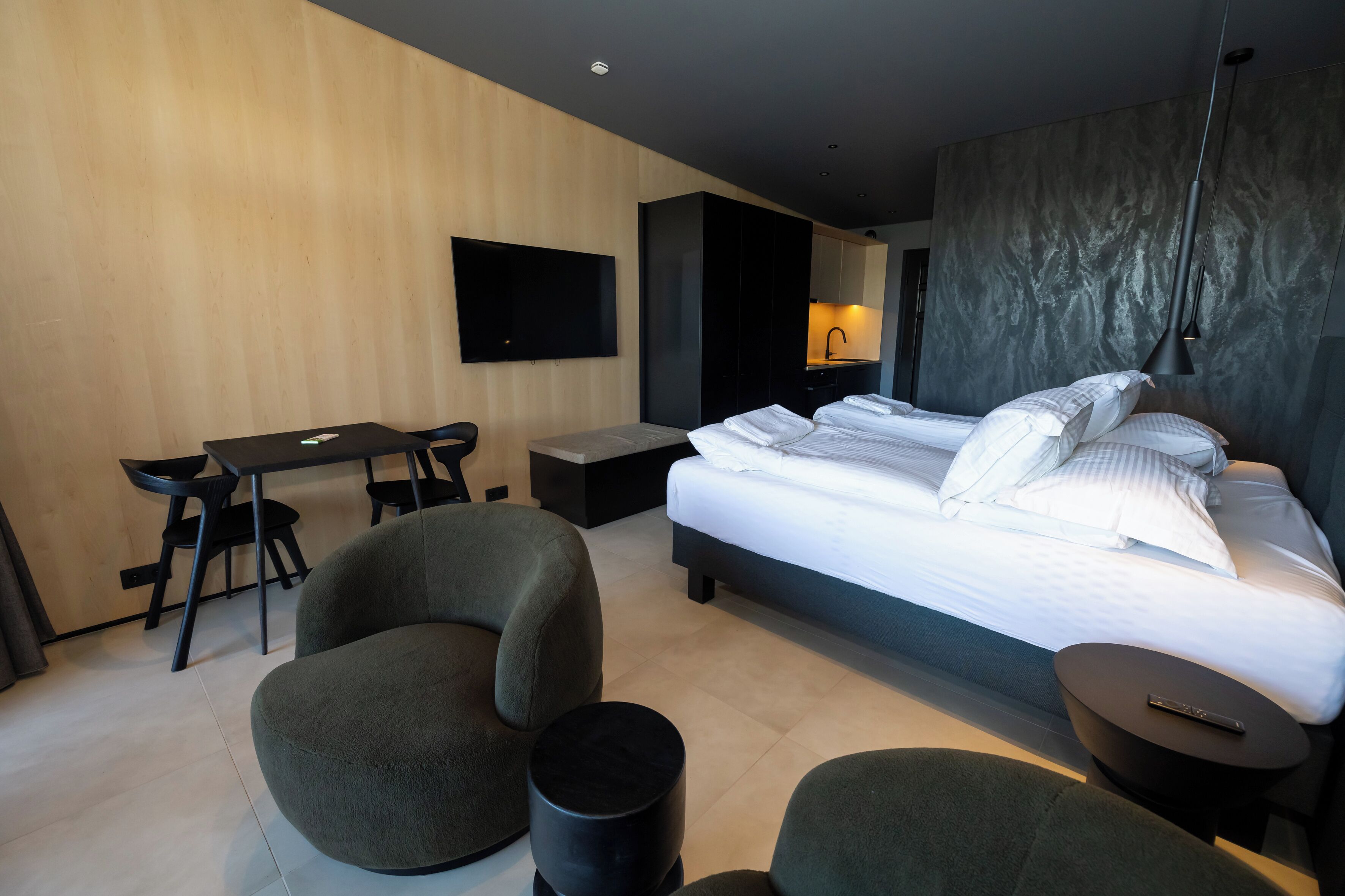 Een moderne hotelkamer met een groot bed, een bureau, twee fauteuils, een bijzettafeltje en een tv aan de muur.