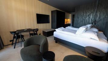 Een moderne hotelkamer met een groot bed, een bureau, twee fauteuils, een bijzettafeltje en een tv aan de muur.