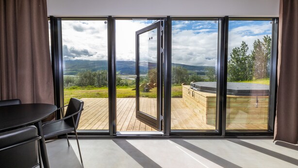A modern room with a large sliding glass door leading to an outdoor deck with a wooden floor and a barbecue area. - North Mountain View Suites (Akureyri)