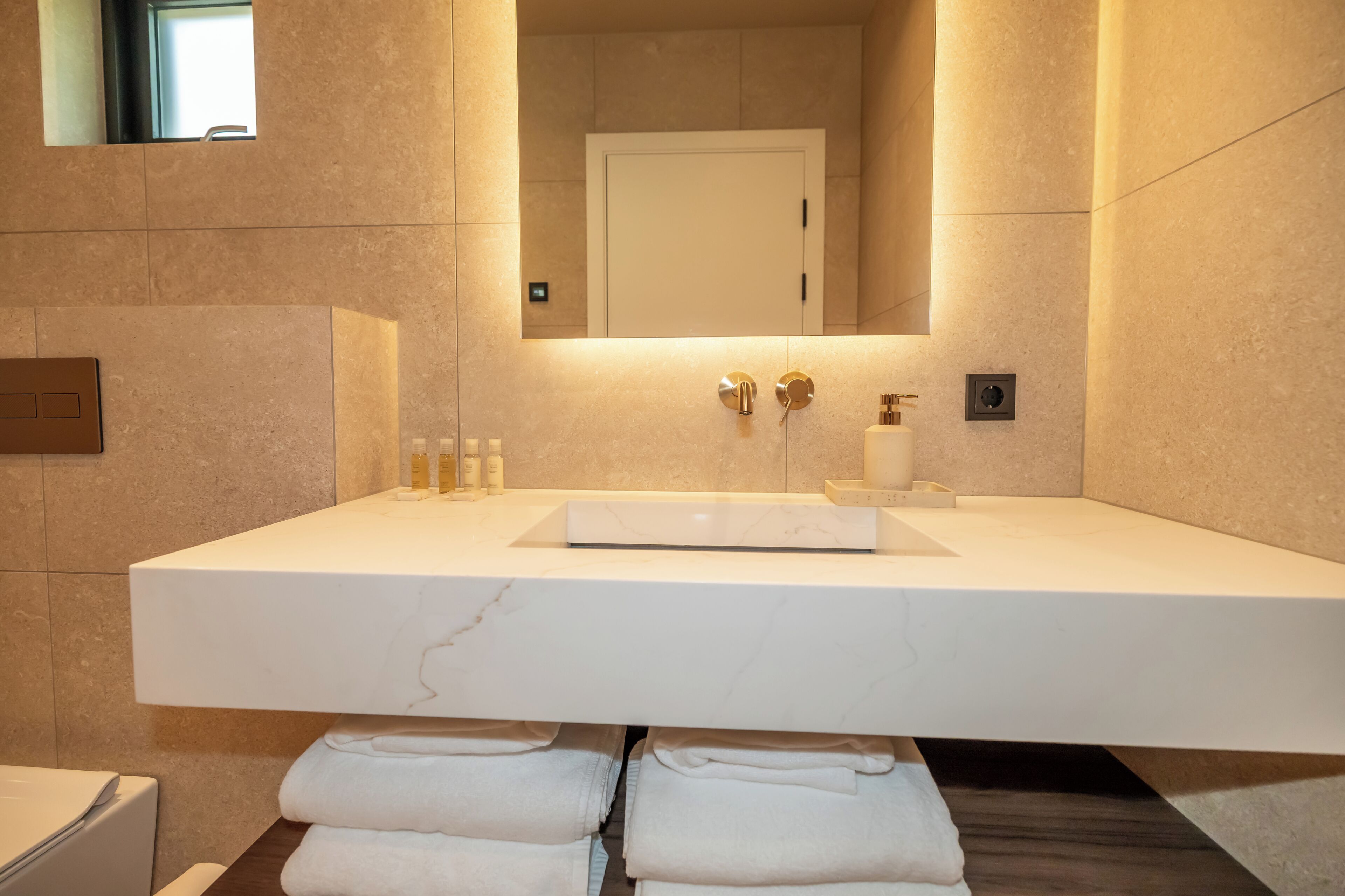 Ein modernes Badezimmer mit einem großen, weißen Marmorwaschbecken, einem Spiegel darüber und einem Handtuchhalter mit gefalteten Handtüchern.